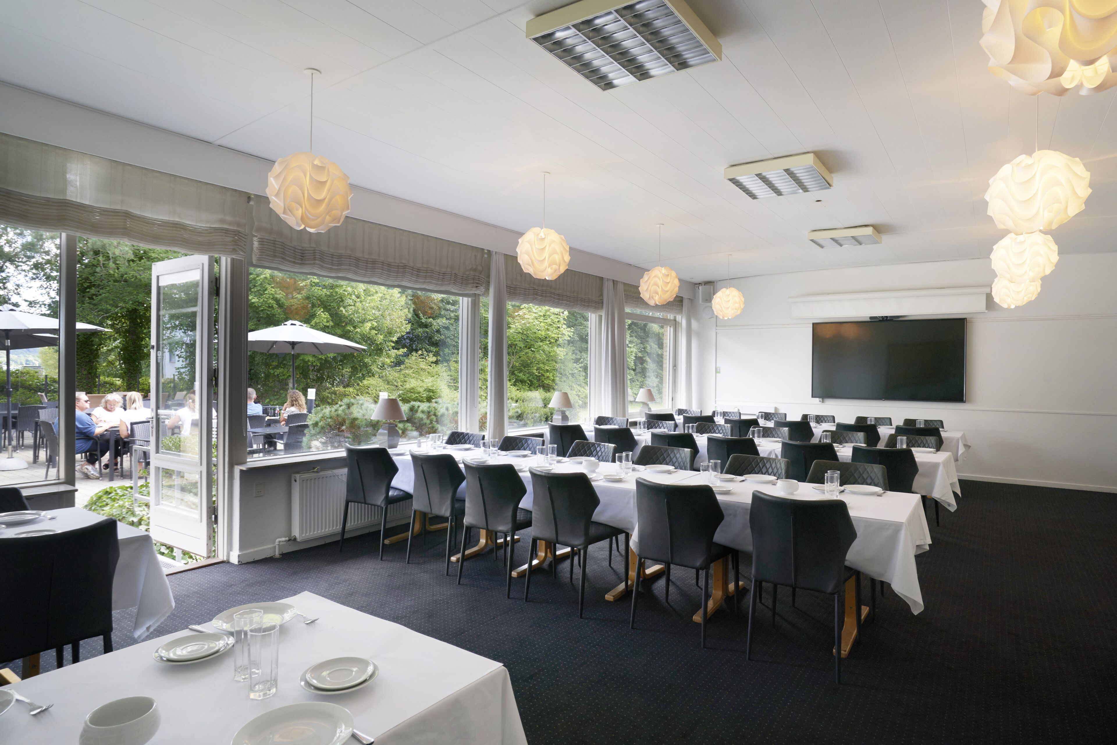 A conference room with tables set for a meeting, large windows, and a flat-screen TV on the wall.