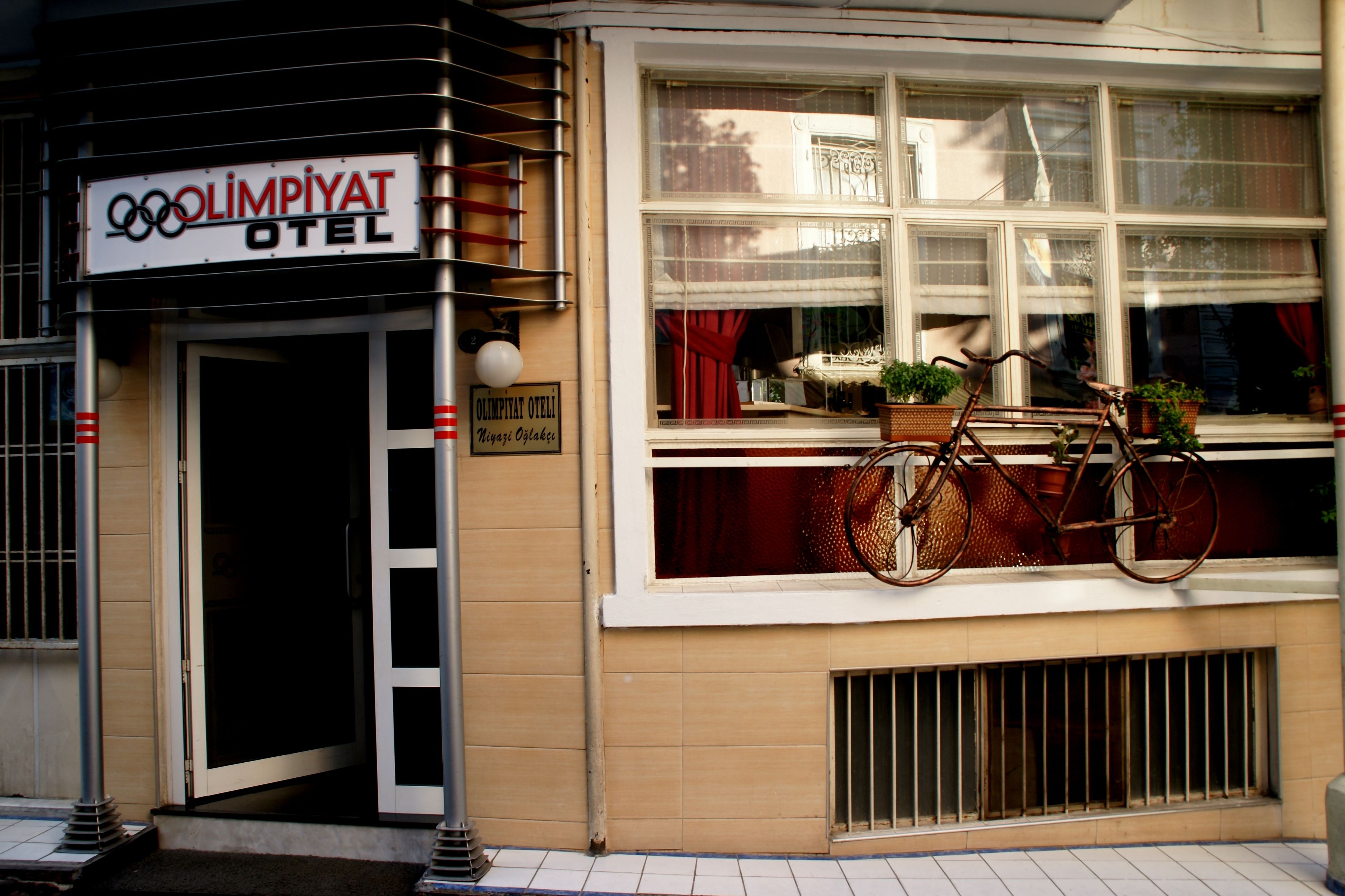 A hotel entrance with a sign reading "OLIMPIYAT OTEL" and a bicycle parked outside.