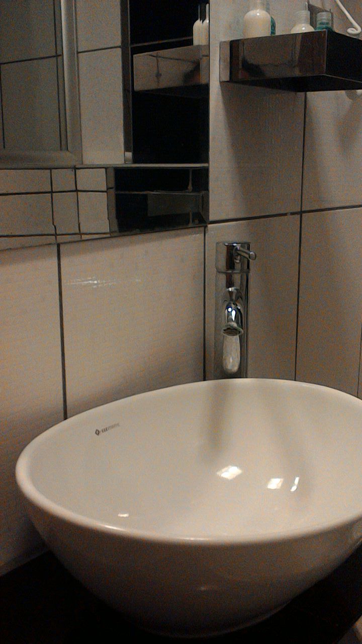 A bathroom with a large white sink, a mirror, and a shelf with toiletries.