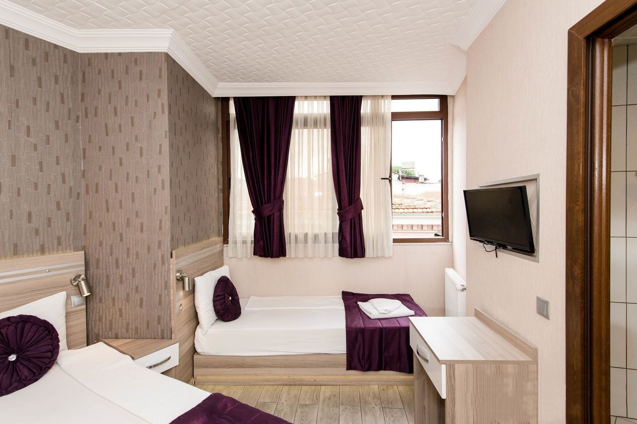 A hotel room with two beds, a TV, a desk, and a window with curtains.