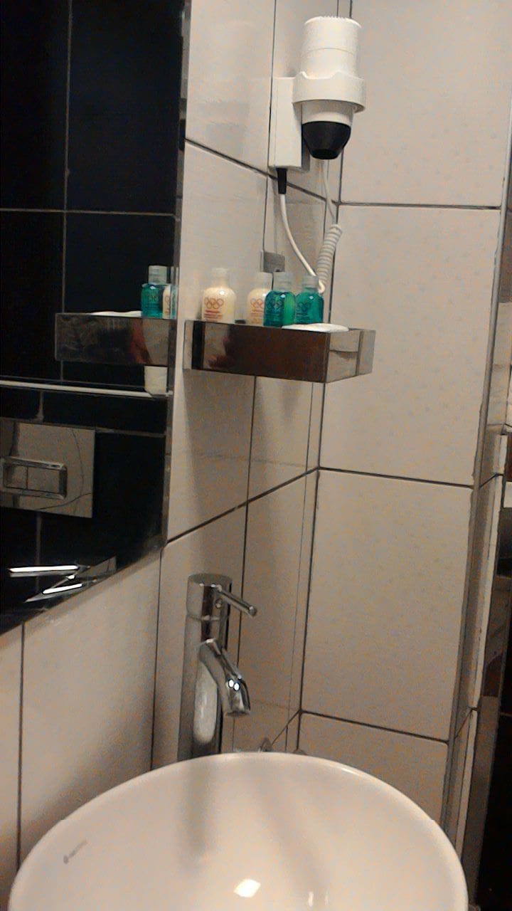 Ein Badezimmer mit einem weißen Waschbecken, einem Spiegel, einem Handtuchhalter und einem Ablagefach für Toilettenartikel.