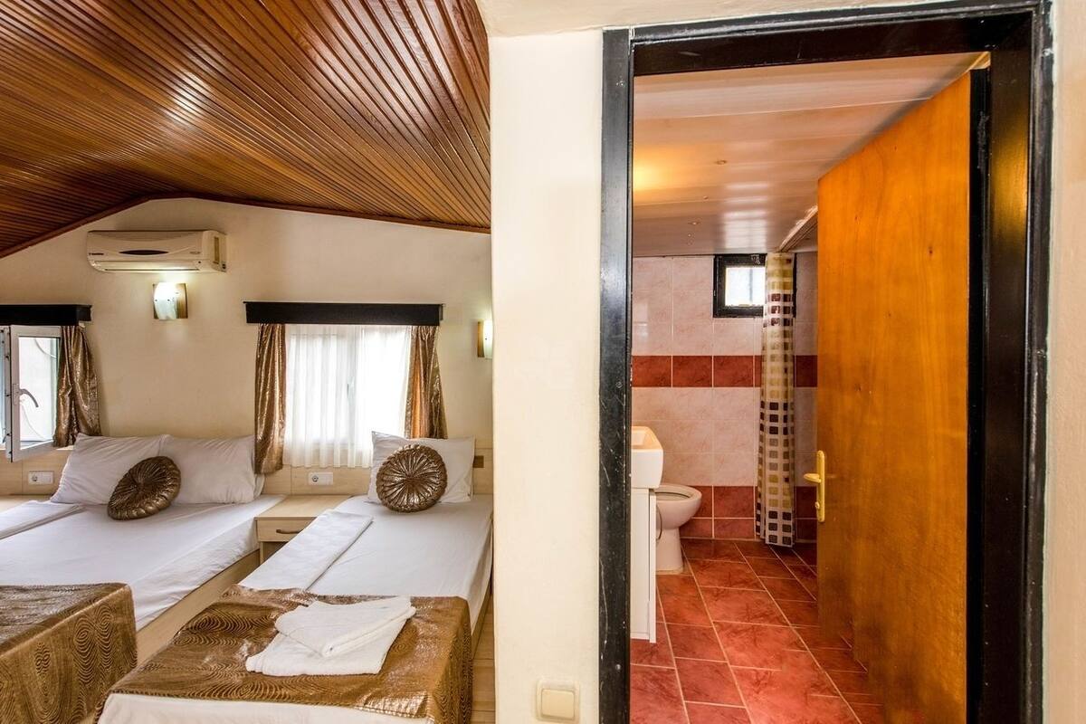 Et hotelværelse med to senge, træloft, klimaanlæg og et badeværelse med toilet og bruser.