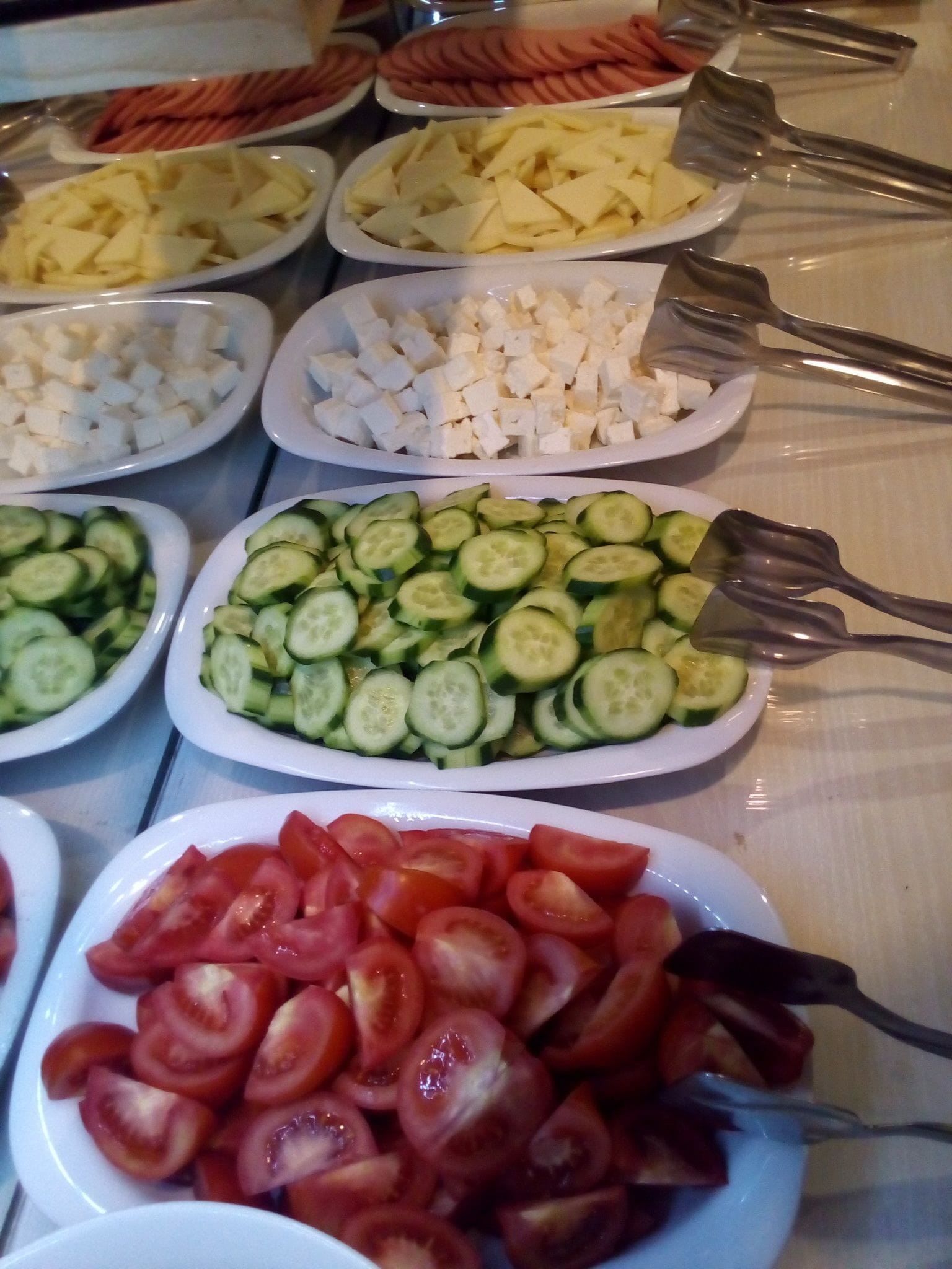 A buffet table with various food items including sliced cucumbers, tomatoes, cheese cubes, and other vegetables.
