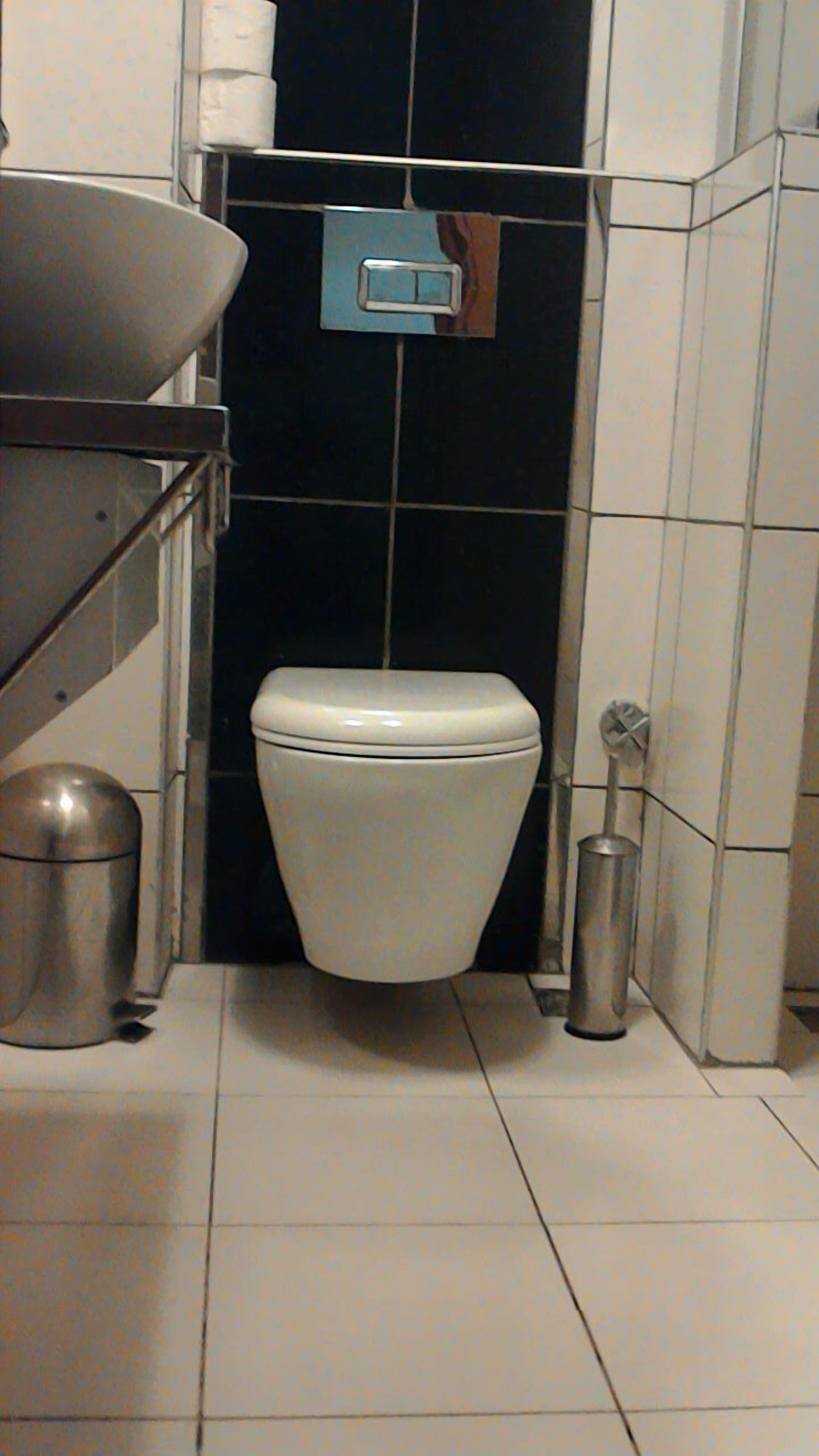 Ein kleines Badezimmer mit Toilette, Mülleimer und einem Handtrockner.