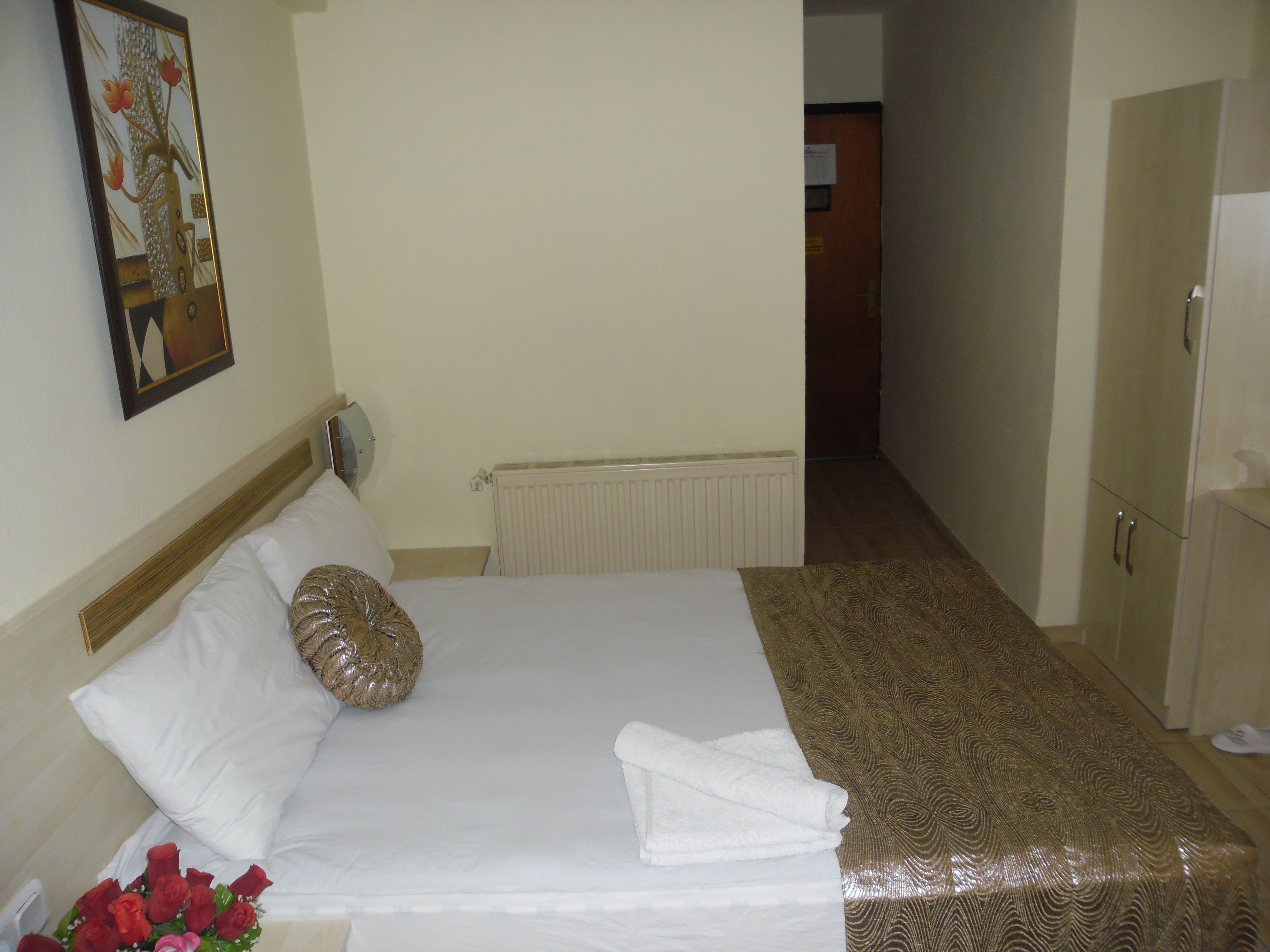 Una habitación de hotel con una cama bien hecha, un radiador, un cabecero de madera, un espejo fijado a la pared y una puerta que da a otra habitación.