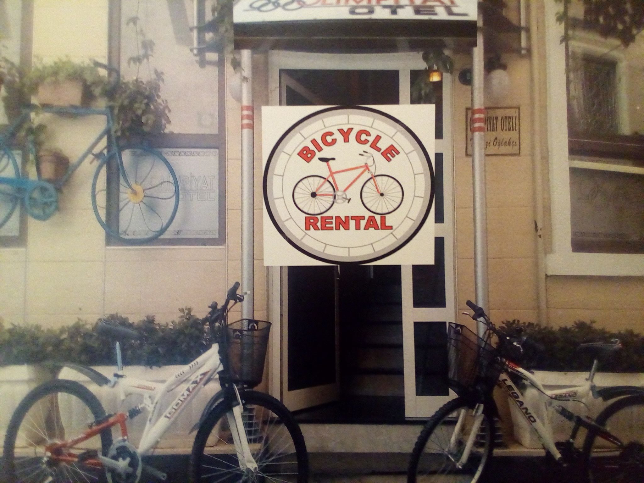 A bicycle rental sign in front of a building with two bicycles parked outside.