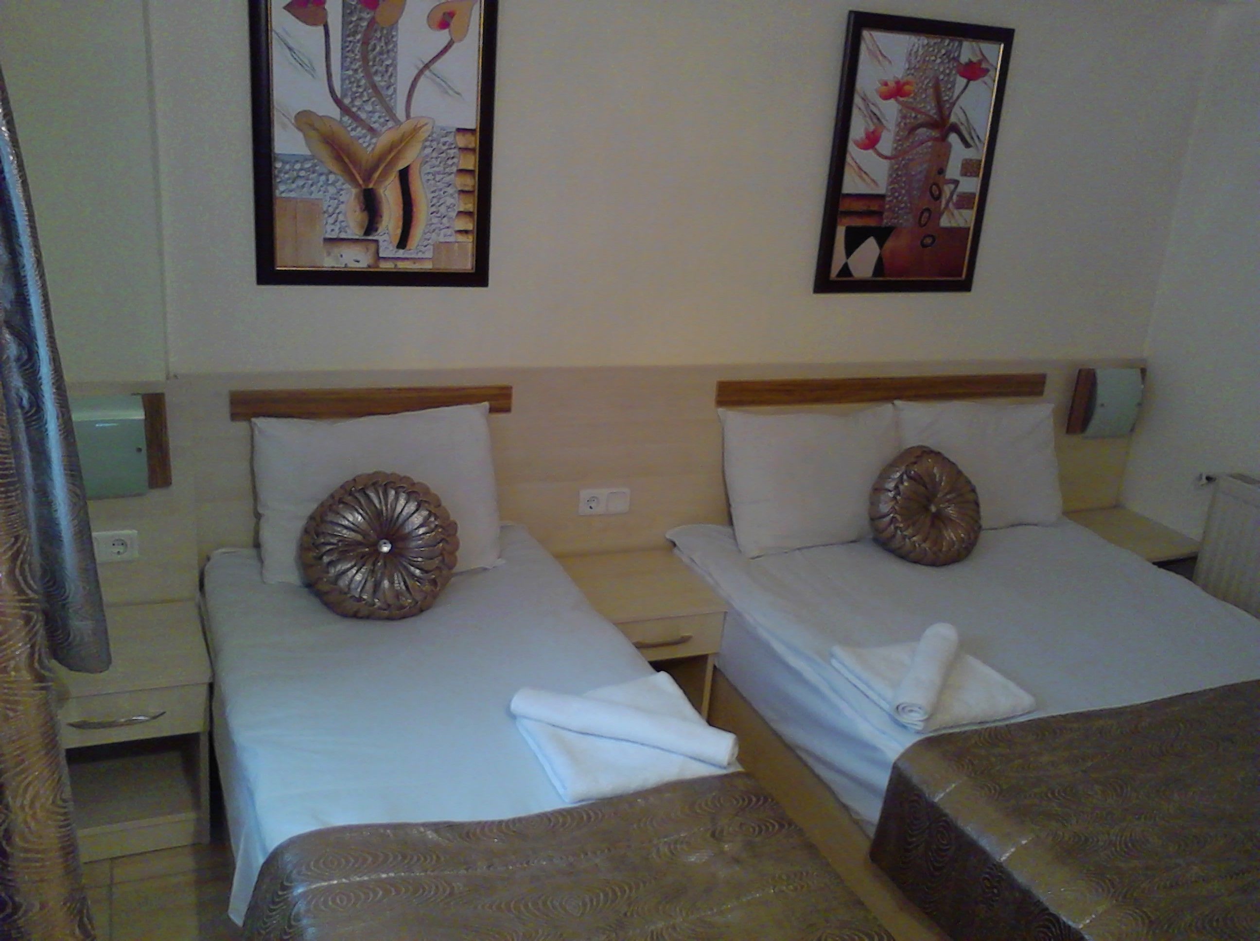 Une chambre d’hôtel avec deux lits, chacun équipé d’un oreiller et d’une petite table de chevet. Deux tableaux sont accrochés au mur, et il y a une table de chevet et une lampe de chaque côté des lits.