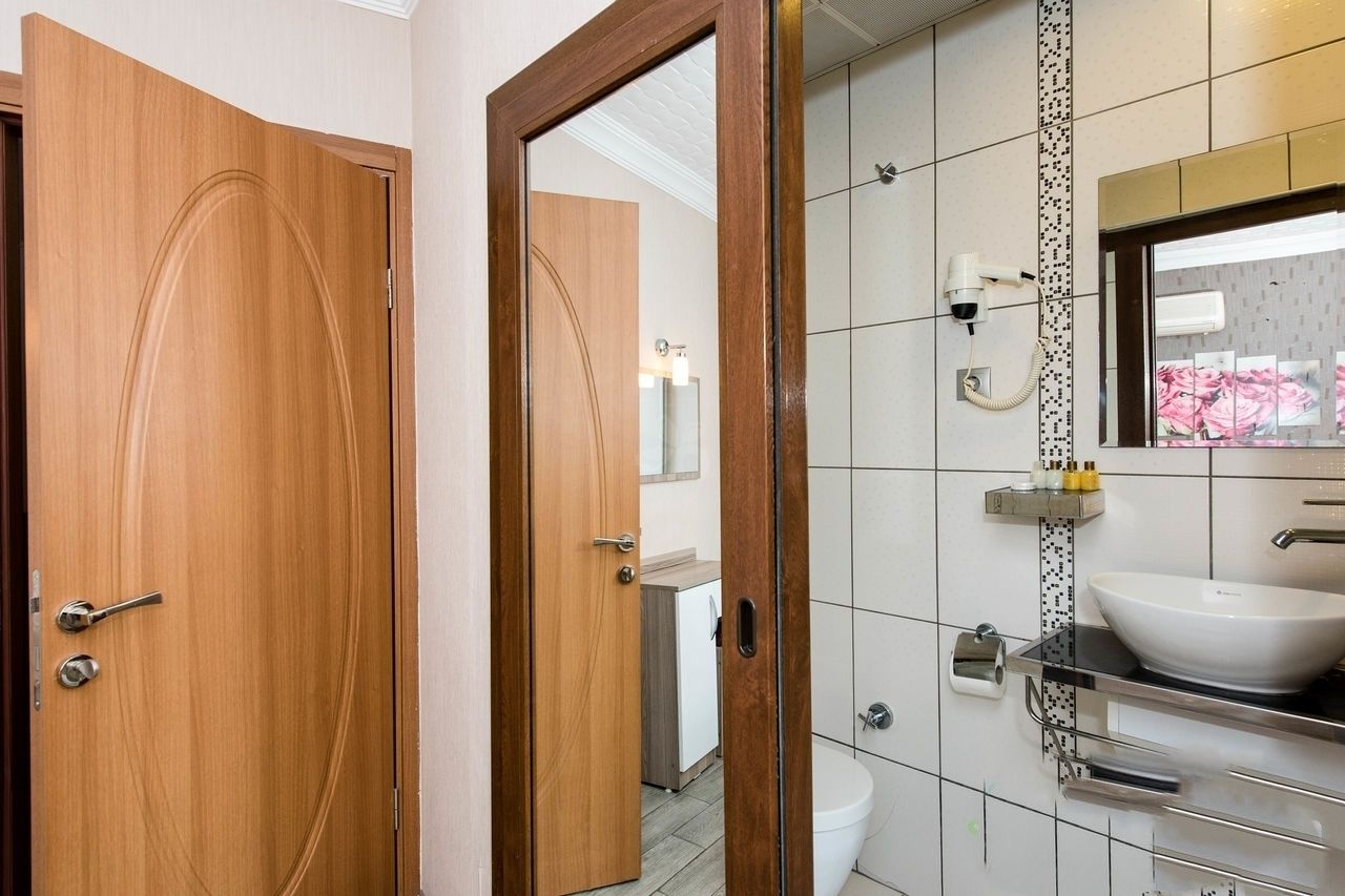 A modern bathroom with a wooden door, a white sink, and a mirror with a floral design.