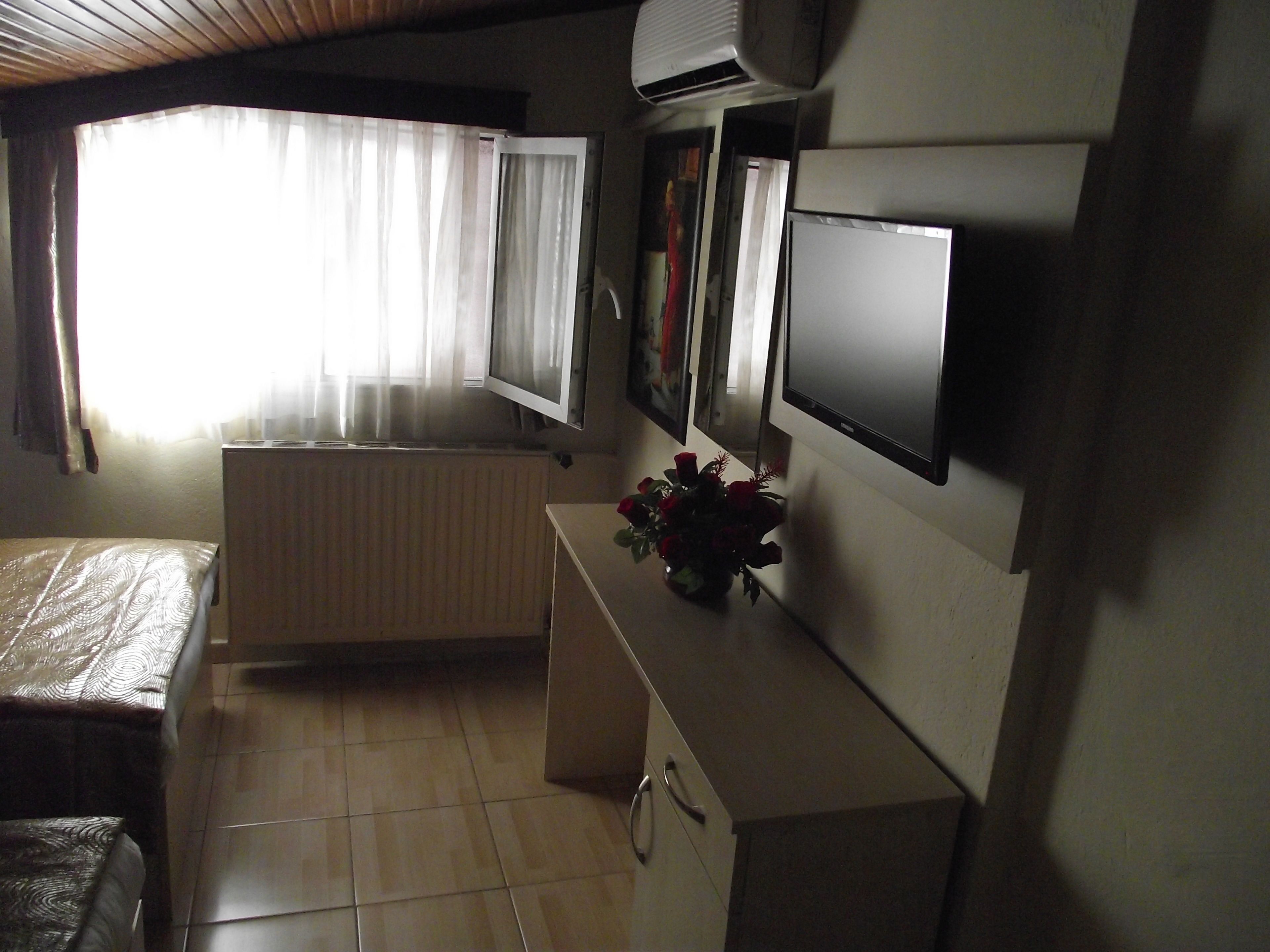 Una stanza piccola e scarsamente illuminata con un letto, un termosifone, una televisione e una finestra con tende.