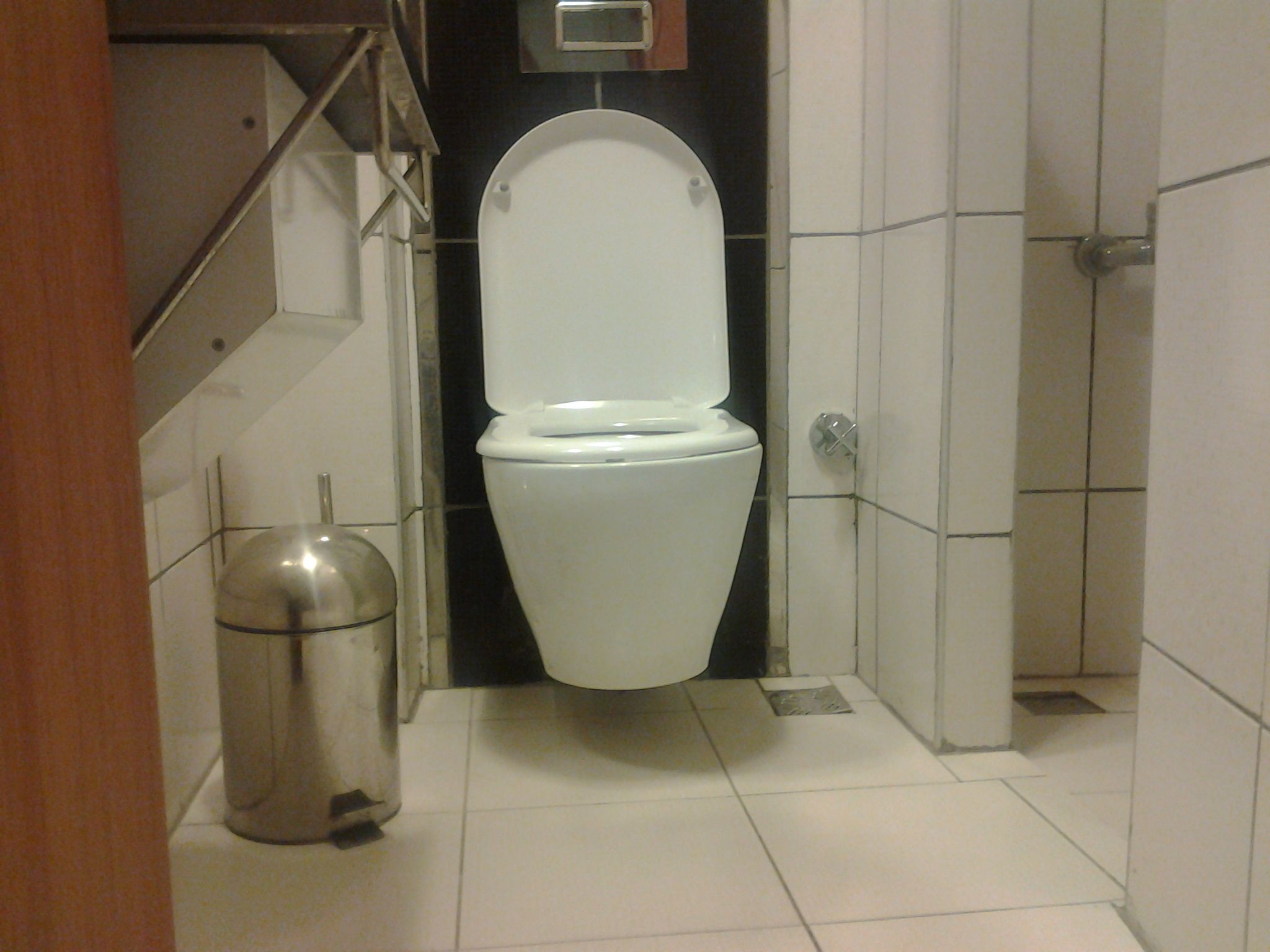 A small, clean bathroom with a white toilet, a trash can, and tiled walls.
