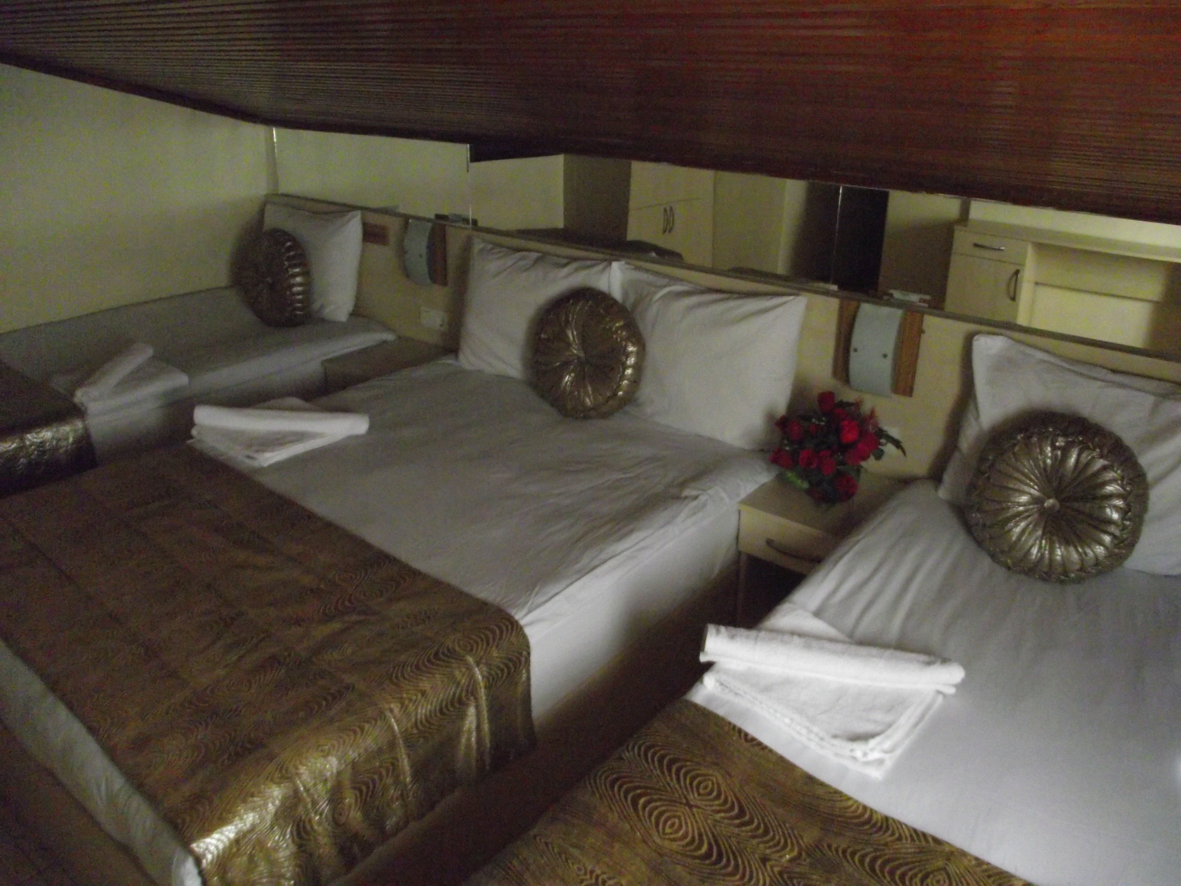 A hotel room with two beds, each with a different patterned bedspread. There is a nightstand with a vase of red flowers and a mirror above the bed.