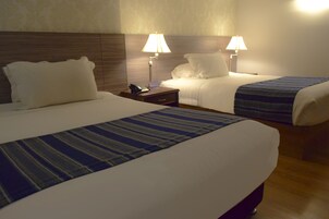 Habitación de hotel con dos camas, cada una con cubrecama azul a rayas, ropa de cama blanca y lámparas de noche.