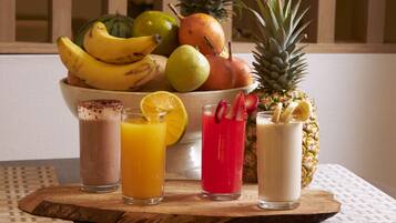 Una tabla de madera con cuatro bebidas, un cuenco de frutas y una piña.