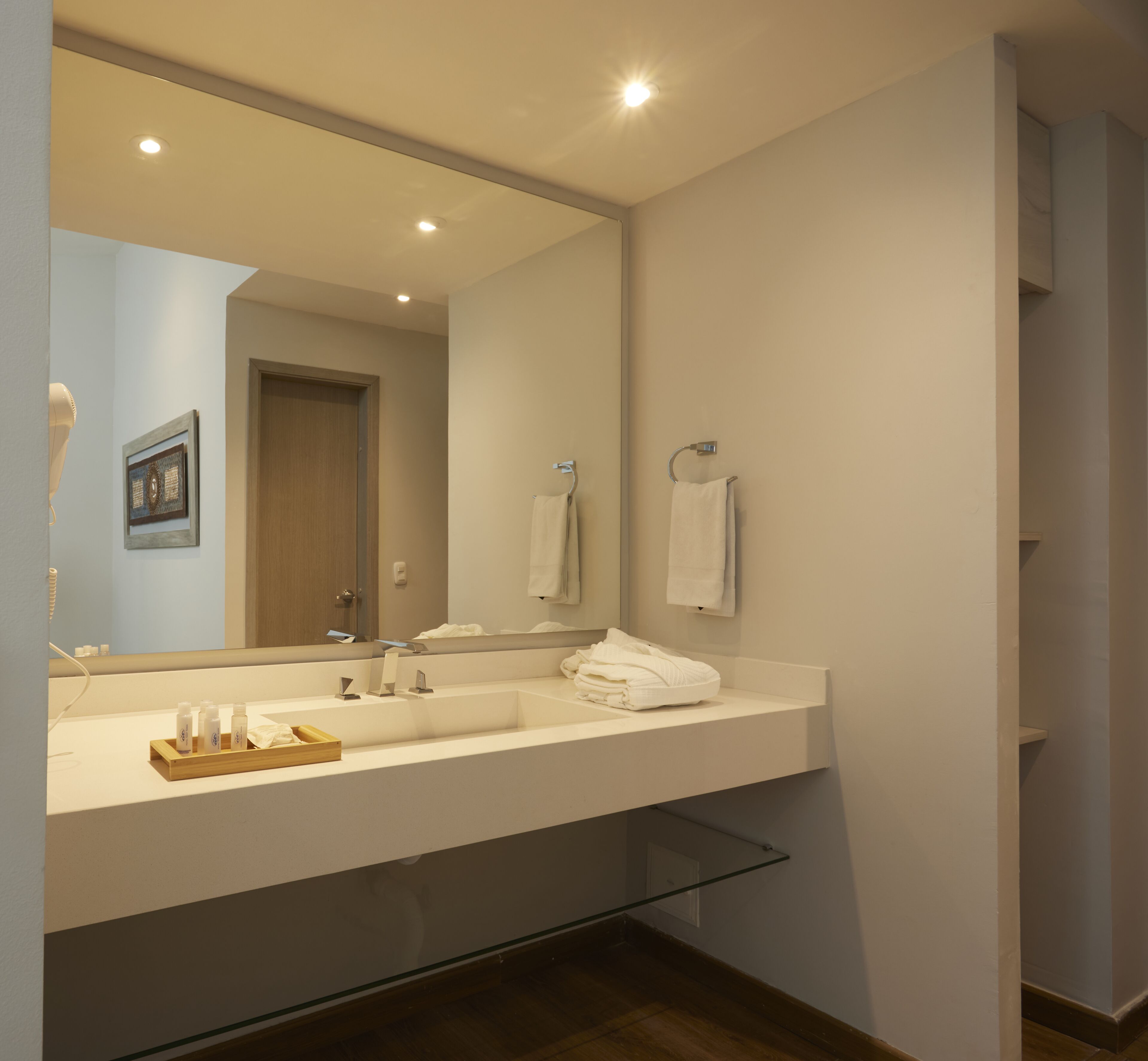 A modern bathroom with a large mirror, a white sink, and a wooden tray with toiletries.