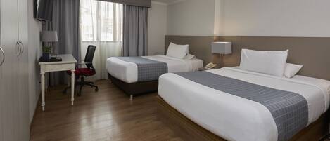Habitación de hotel con dos camas, un escritorio con silla, televisión y ventana con cortinas.