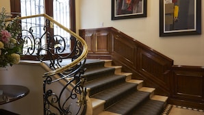 A grand staircase with a curved design, a chandelier, and framed artwork on the walls. - Hotel Saint Simon (Bogotá)