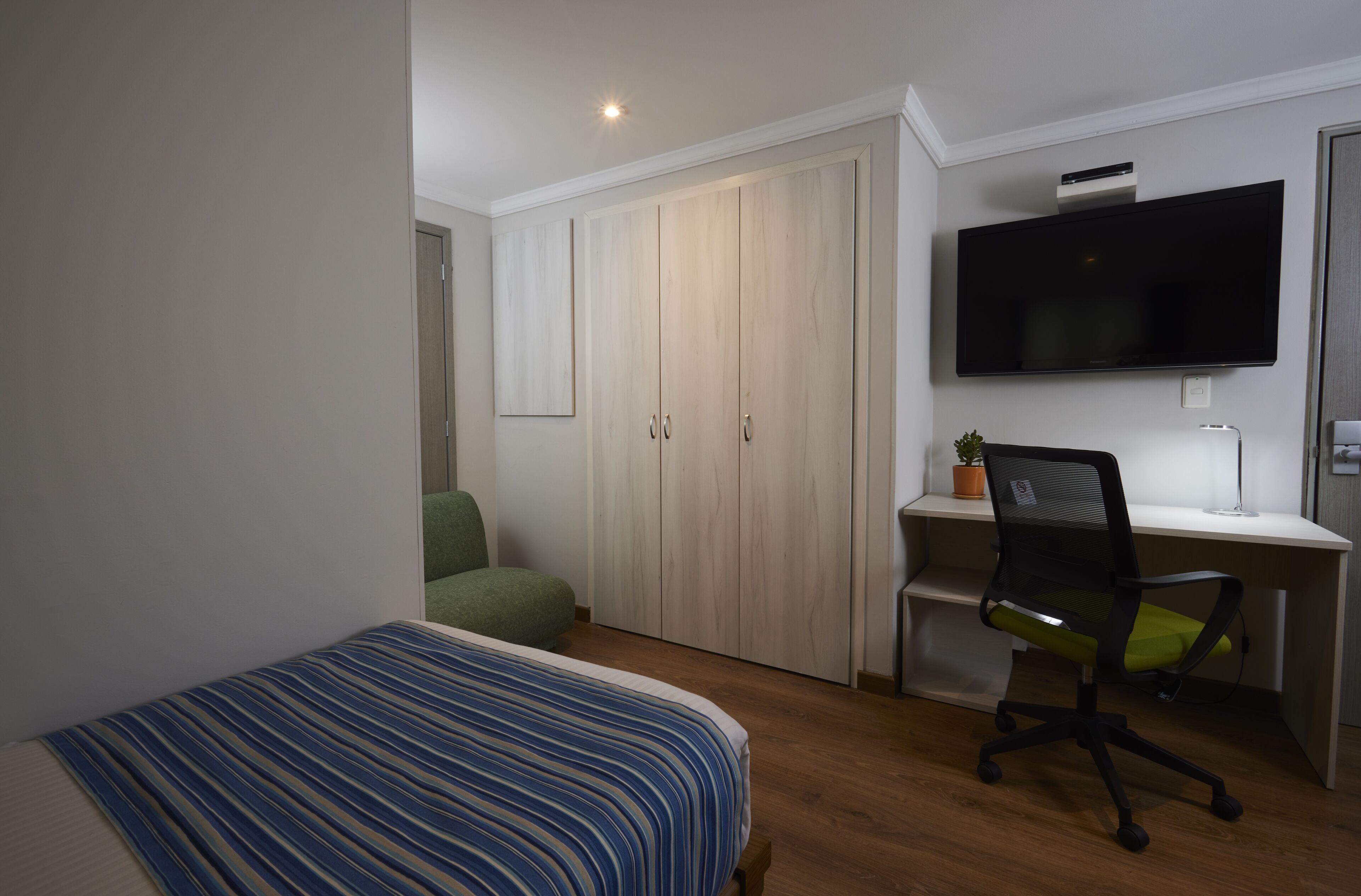 Un dormitorio con cama, un escritorio con silla, un televisor y un armario.