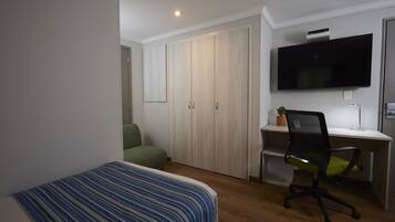 A bedroom with a bed, a desk with a chair, a television, and a wardrobe.