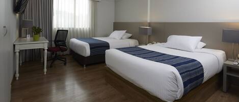 A hotel room with two beds, a desk with a chair, a TV, and a lamp.