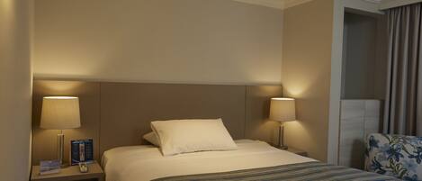 A hotel room with a large bed, two bedside lamps, a nightstand, and a chair with a floral pattern.