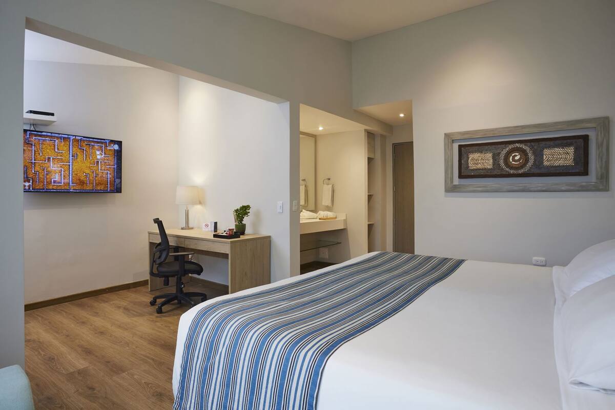 A hotel room with a bed, desk, chair, and a bathroom visible through an open door.