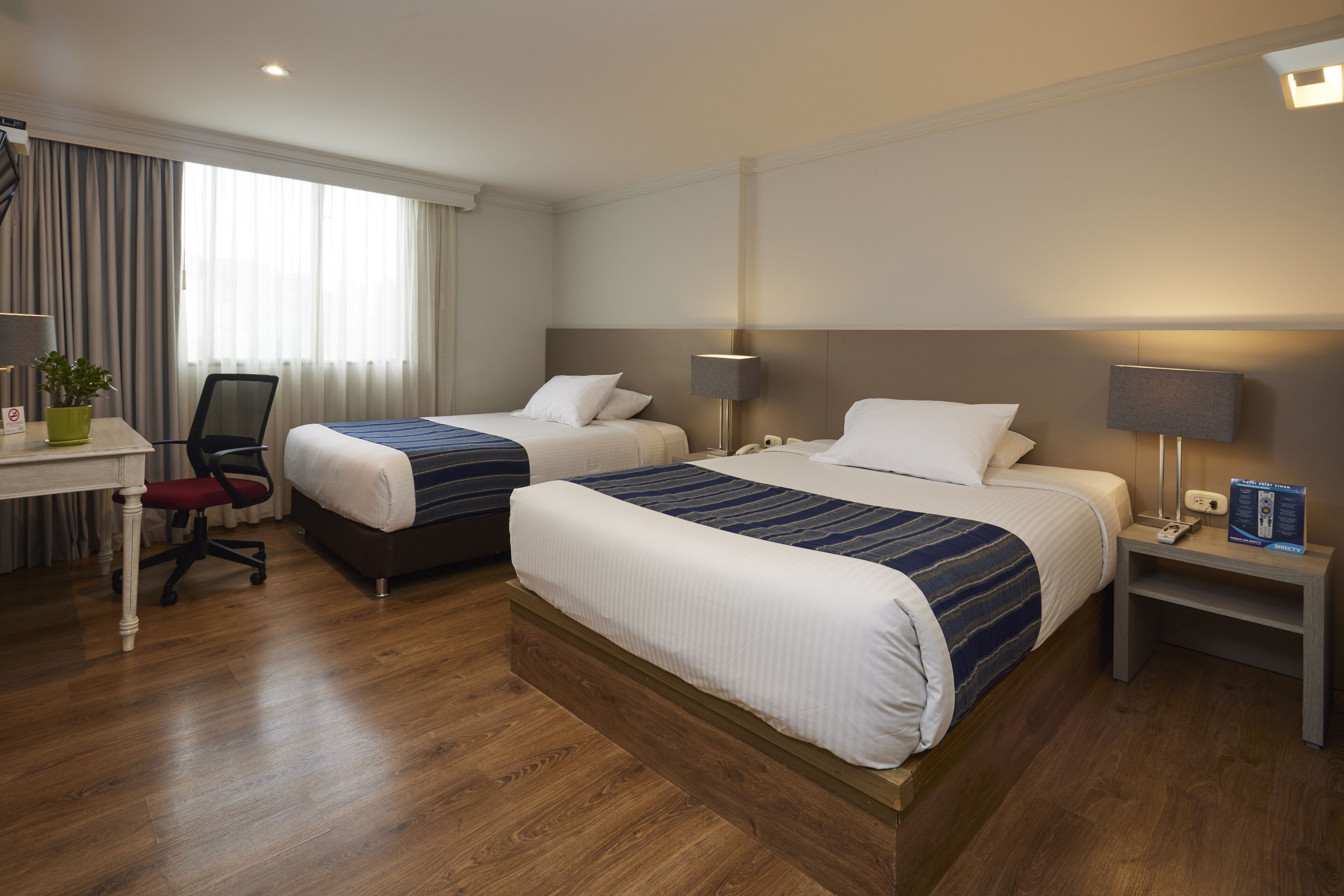 A hotel room with two beds, a desk, and a chair.