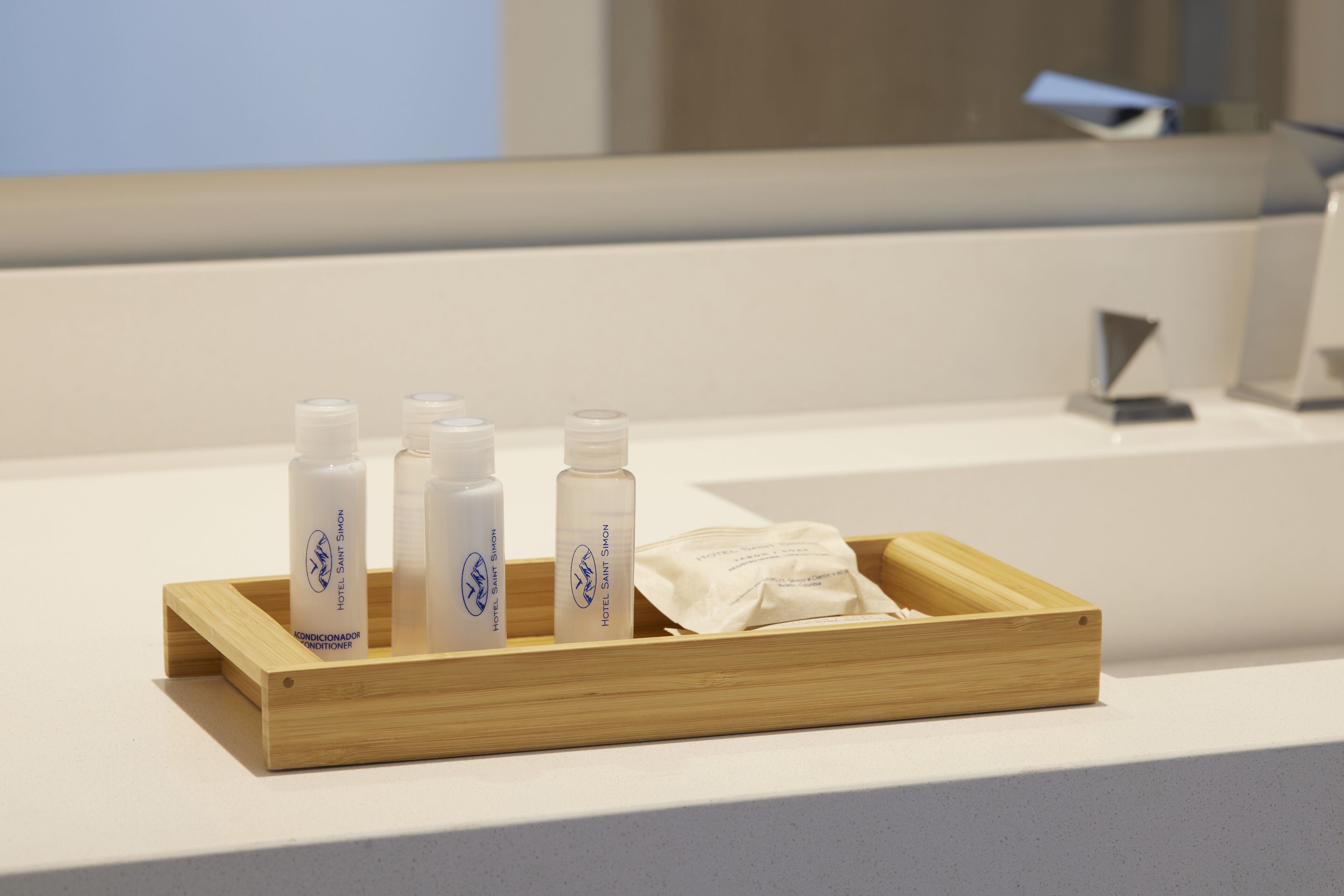 A wooden tray with four bottles of hotel amenities and a folded towel on a white countertop.