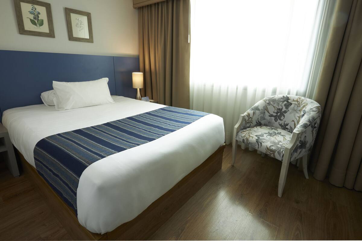 A hotel room with a large bed, a chair, a nightstand, and a window with curtains.