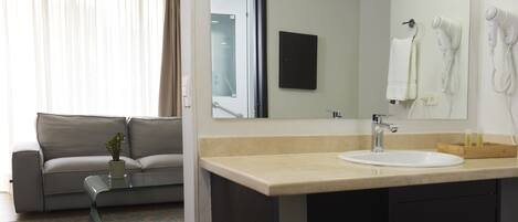 A hotel room with a sofa, a glass coffee table, a sink, and a mirror.