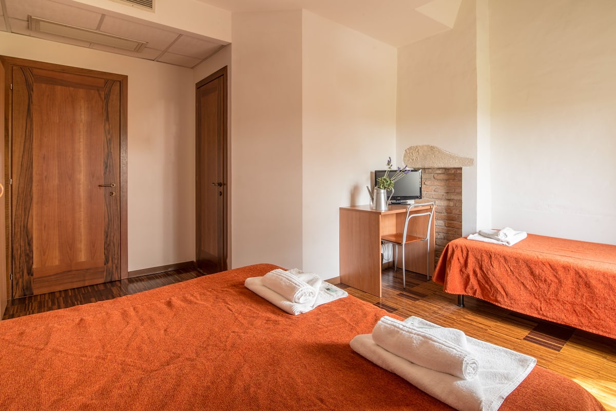 A hotel room with two beds, a desk, a television, and a fireplace.