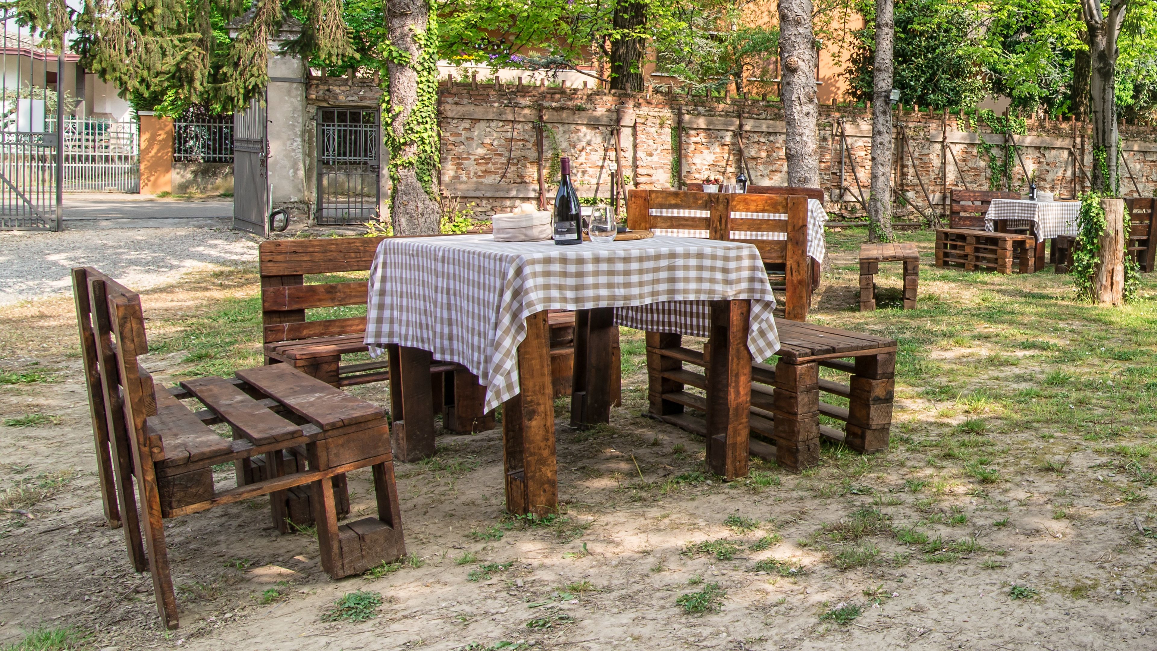 Ein Holz-Garnitur mit Tisch und Stühlen steht auf unbefestigtem Boden, bedeckt mit einer karierten Tischdecke.