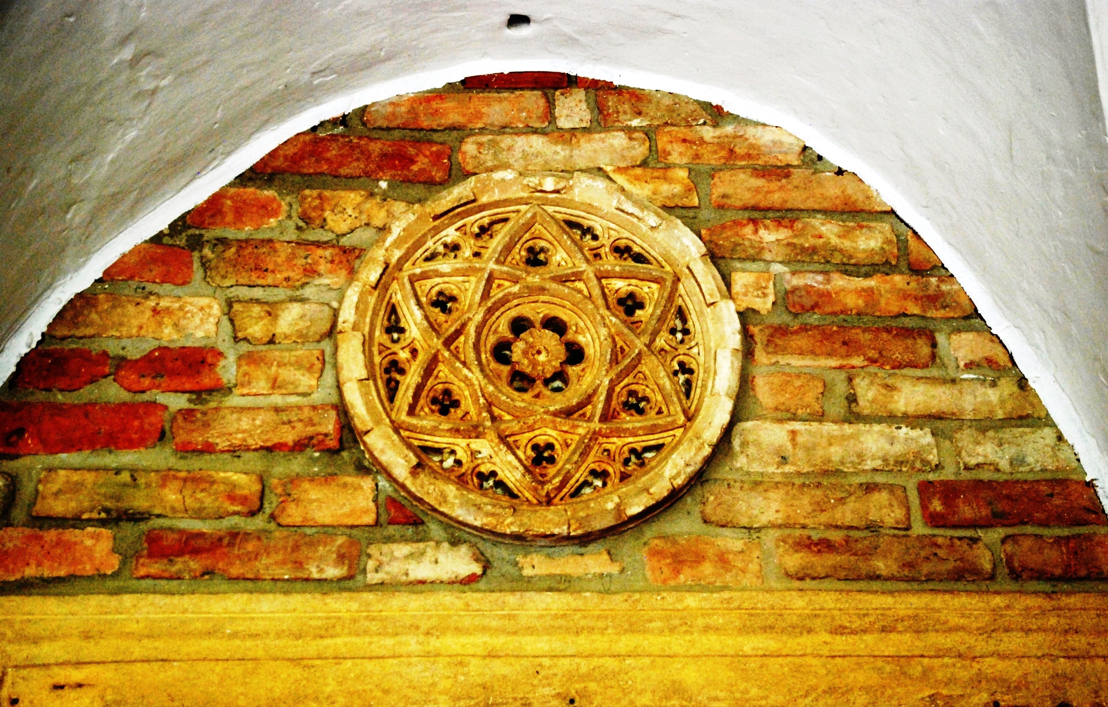 Un muro de ladrillo con una placa metálica circular y ornamentada.