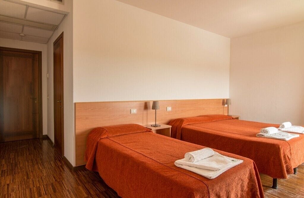 Ein Hotelzimmer mit zwei Betten, Holzboden, einem Holzkopfende und einem Nachttisch mit Lampe.