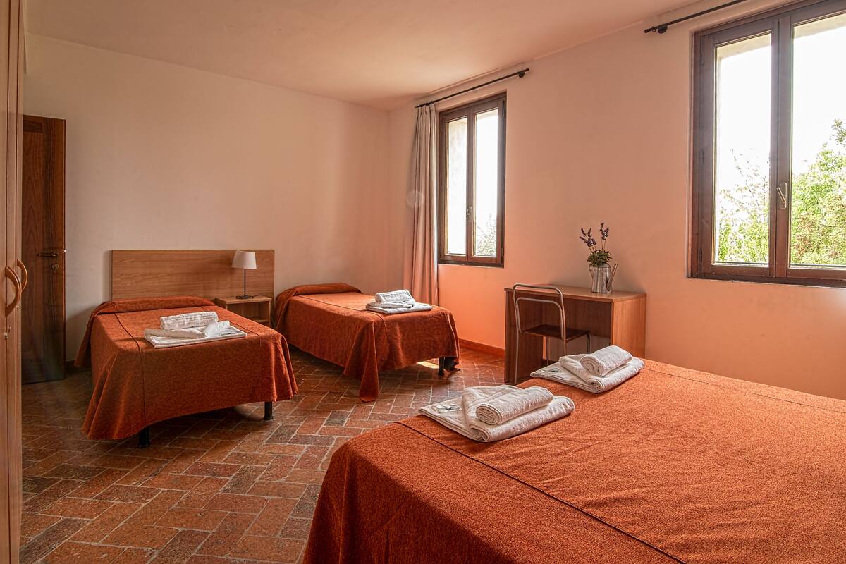 A hotel room with two beds, a small desk, a chair, and a window with curtains.