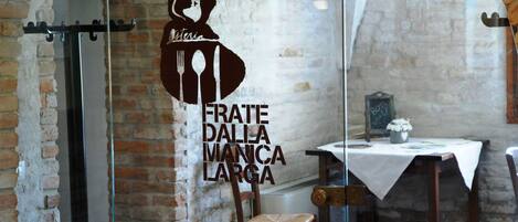 Interior de un restaurante con pared de ladrillo rústico, una división de vidrio y una mesa dispuesta para comer.