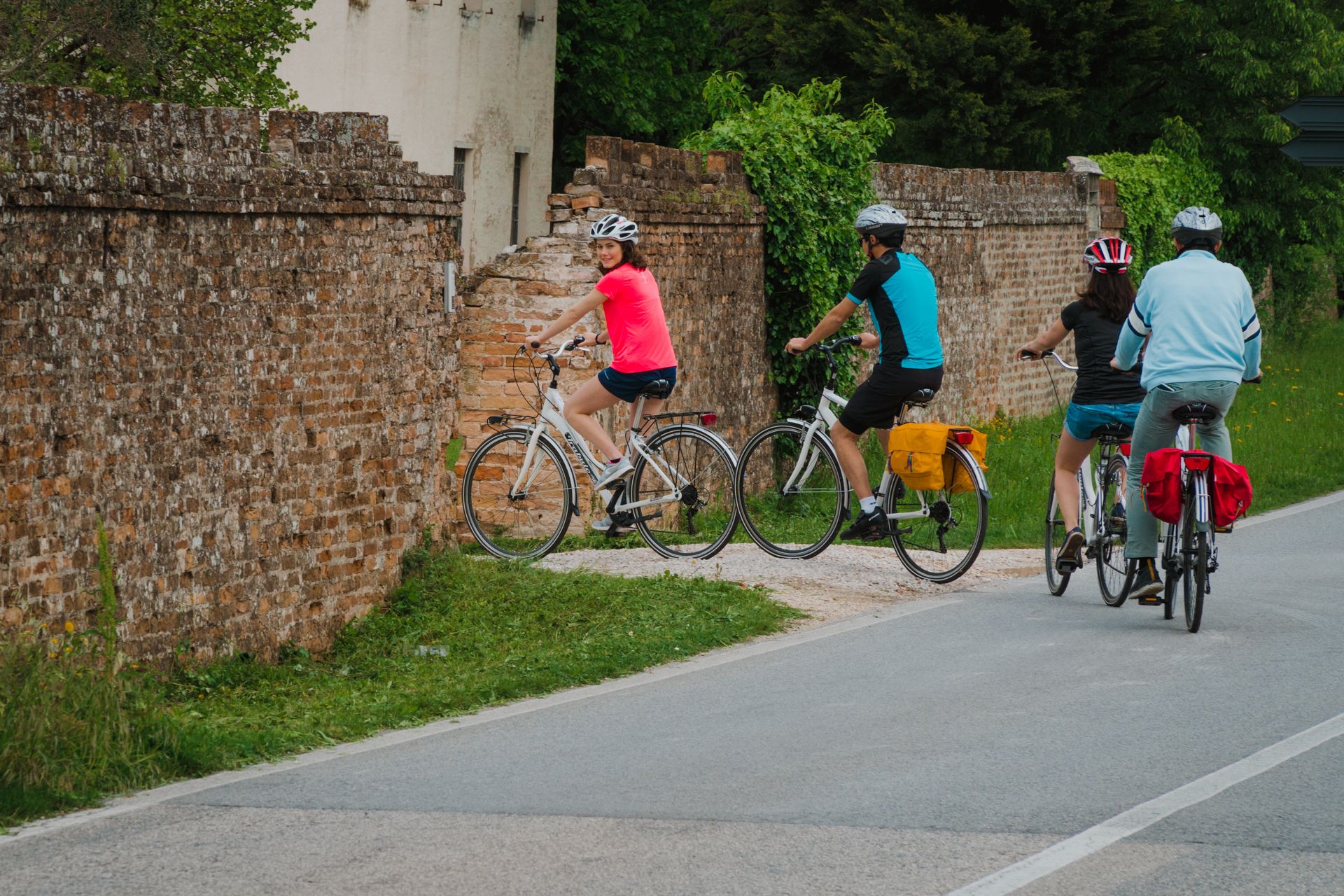 A paved path with cyclists, a brick wall, and greenery.
