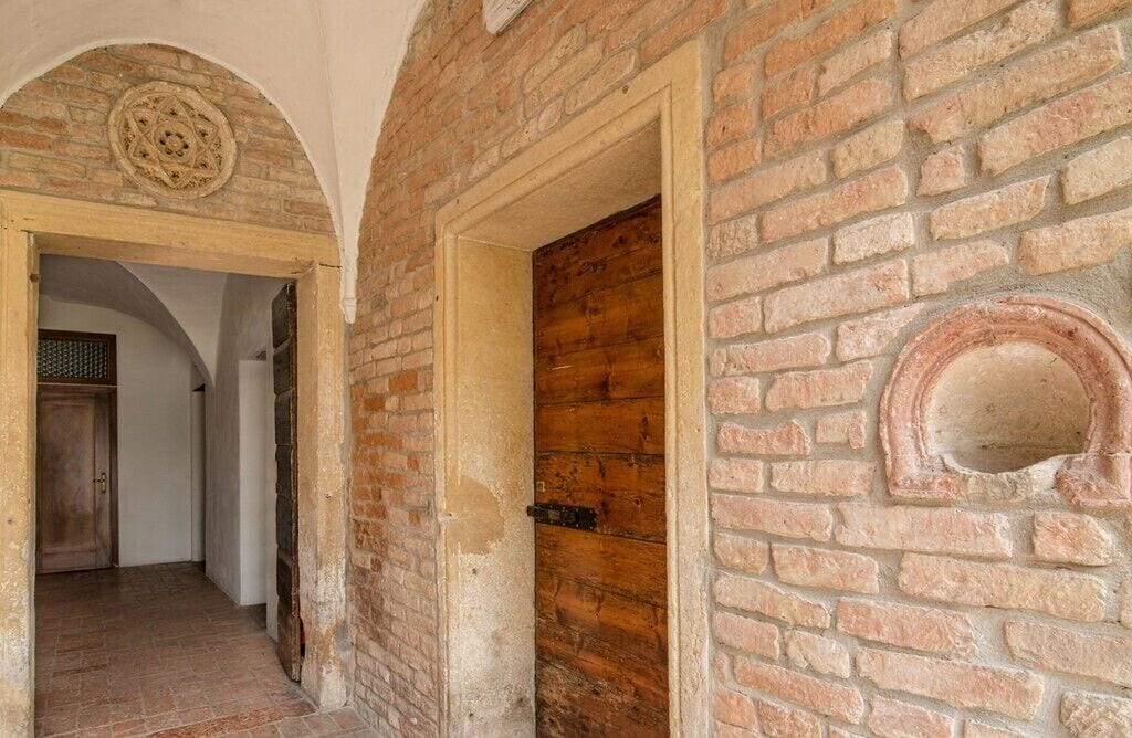 Un couloir aux murs en briques apparentes, avec une porte en bois et une fenêtre ronde.
