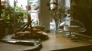 A table with a cake on a glass stand, a basket of bread, and a vase of flowers by a window. - Hostellerie Du Lys - Hôtel & Restaurant (Lamorlaye)