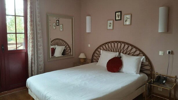 A bedroom with a large bed, a wooden headboard, a bedside table with a lamp, a mirror, and framed pictures on the wall. - Hostellerie Du Lys - Hôtel & Restaurant (Lamorlaye)
