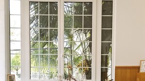 A round wooden dining table set with glasses and a vase, positioned in front of a window with a view of palm trees. - Hostellerie Du Lys - Hôtel & Restaurant (Lamorlaye)