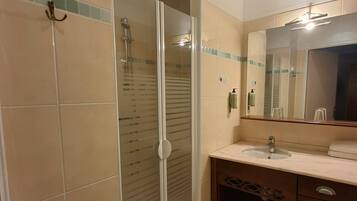 Une salle de bain avec une douche à parois de verre, un lavabo avec un miroir et un sol carrelé.