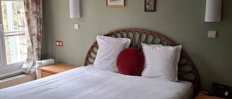 A neatly made bed with white linens and a red pillow, flanked by wooden nightstands with a telephone and a lamp.