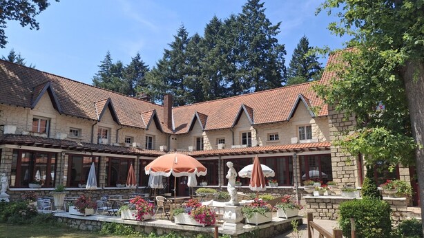 A courtyard with stone buildings, outdoor seating, and a statue. - Hostellerie Du Lys - Hôtel & Restaurant (Lamorlaye)