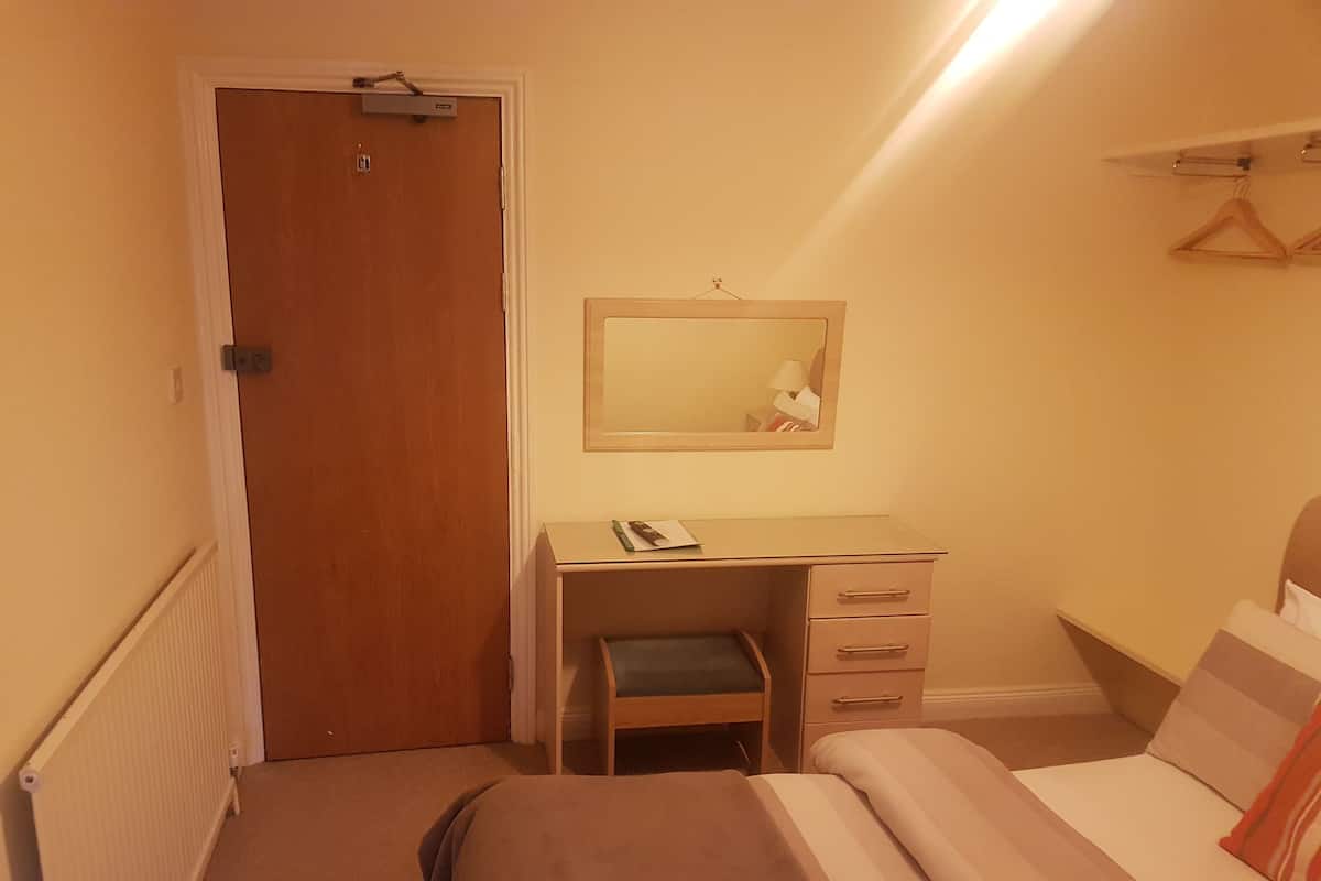 A bedroom with a bed, a desk with a chair, a dresser, a mirror, and a door.