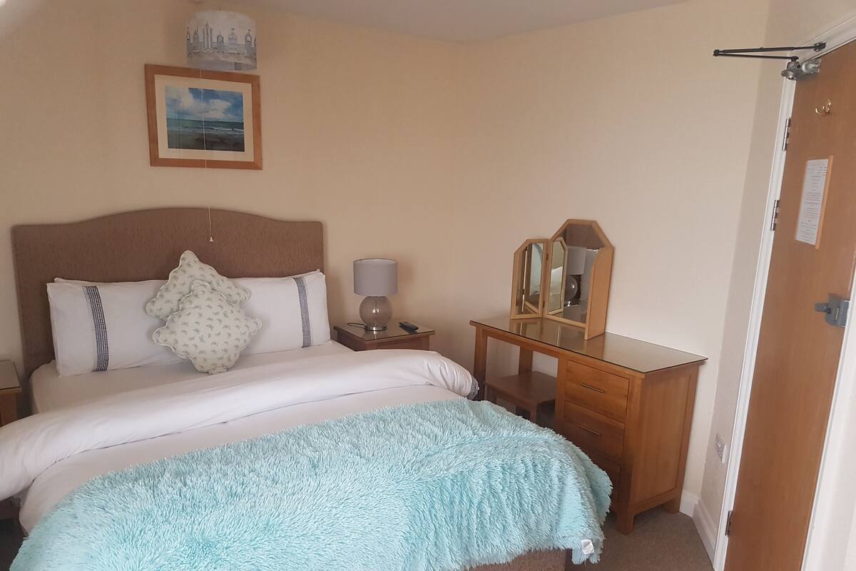 A neatly arranged bedroom with a bed, bedside table, lamp, and a wooden dresser.