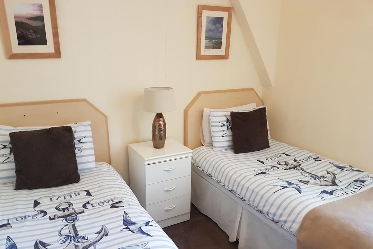A twin bedroom with two beds, each with a striped bedspread featuring nautical themes. There is a bedside table with a lamp between the beds.
