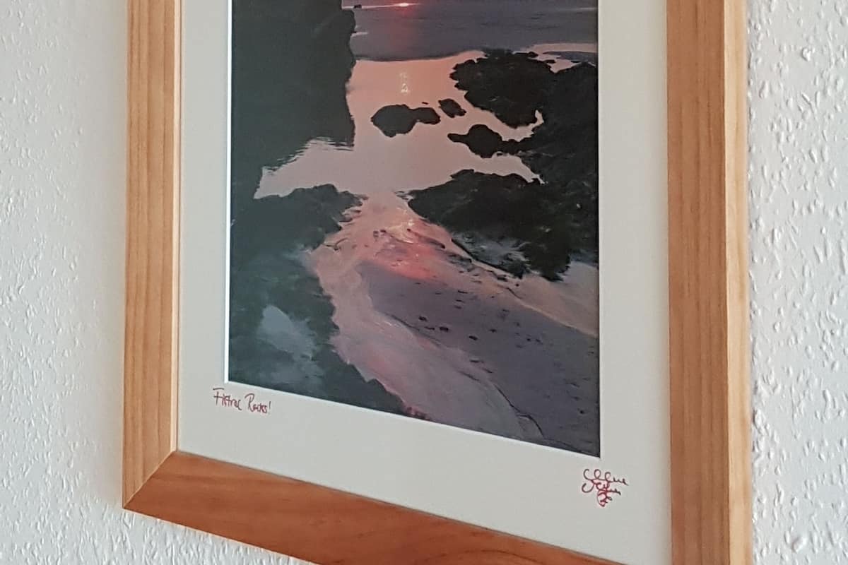 A framed artwork of a sunset over a rocky shoreline.