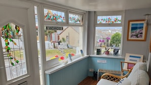 A cozy room with a wicker sofa, a window with a 'Vacancies' sign, and a view of the street. - Trelinda Hotel (Newquay)