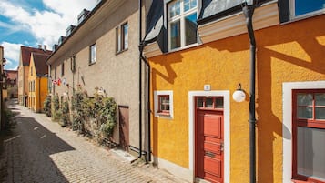 A narrow cobblestone street lined with traditional European buildings, featuring a prominent yellow facade with a red door and a small window.