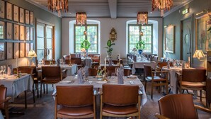 A restaurant with multiple dining tables, chairs, and hanging light fixtures. - Hotell Lindgården (Visby)